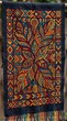© MD - Handwoven textile with intricate tribal patterns and vibrant leaf motifs in warm colors on dark fabric