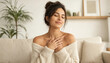 © ARMAN - Young South Asian woman in white robe holding chest smiling peacefully at home
