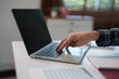 © Tj - Hand typing on a laptop keyboard, holding a pen while working efficiently on a white desk, representing concepts of productivity, remote work, and digital communication