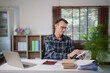 © Tj - Mature man calculating finances at home office desk, using calculator and laptop for accounting, reviewing paperwork, managing budget and taxes
