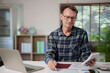 © Tj - Senior man analyzing financial documents and bills with a calculator at home, managing personal budget, planning taxes, and calculating expenses for retirement savings and investments