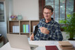 © Tj - Mature man in glasses working remotely on laptop from home, having a video conference, engaging in online learning, or participating in a virtual meeting