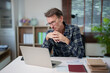 © Tj - Senior man working on laptop at home office, concentrating on business tasks, thinking about financial data, and managing remote work responsibilities