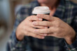 © Tj - Person enjoying a warm takeaway coffee, hands holding a disposable cup, relaxing during a morning break, savoring a hot beverage in a casual setting