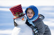 © Volodymyr - Kid decorating snowman with carrot nose in snow. Happy kid building snowman. kid enjoying sunny winter game. Child creating snowman with scarf and funny hat. Kids creativity in winter. New Year card.