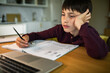 © Davor - Tired boy studying homework with laptop at home