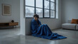 © AlgoCreative - Lonely woman blanket cold home interior winter mood large window concrete floor minimal furniture blue textile empty space sadness solitude Lonely Seasonal affective disorder winter blues concept