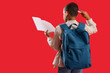 © Pixel-Shot - Thoughtful little schoolboy with backpack and copybook on red background, back view