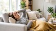 © Ctra - Young woman lying on couch at home, feeling sick with a headache and fever, covered in a warm blanket
