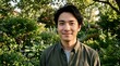 © Eni - Portrait of a smiling young Asian man standing in a lush green garden during golden hour.