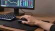 © mihrzn - A hand grips a gaming mouse over a black pad, with a lit keyboard and monitor displaying trading charts in background.