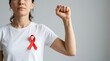 © Dean - Empowered woman wearing red ribbon on white shirt raising clenched fist to show support for world aids day awareness campaigns and medical health support programs and community fight