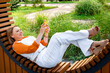 © 5ph - Adult woman on curved wooden bench with smartphone. Urban summer park, leisure time, modern digital communication, comfortable outdoor seating