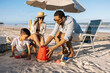 © kleberpicui - A happy family enjoys a sunny beach day as a father helps his son build a sandcastle while the mother relaxes under an umbrella, capturing playful summer moments and seaside bonding by the ocean.