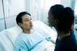© Pixel-Shot - Asian man patient in hospital bed talking with a female visitor, healthcare and medical support