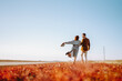 © maxbelchenko - Young man and woman walk together across bright grassy field at sunset. A loving couple in stylish clothing enjoys nature and time together outdoors. Concept of love and relaxation.