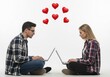 © MdMostafizur - Young couple sitting on the floor using laptops with red hearts floating above them