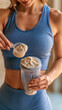 © Treceer - A close-up photograph of a fit woman in blue sportswear preparing a protein shake, holding a shaker bottle and using a scoop to add powder.