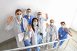 © Pixel-Shot - Team of doctors with medical masks waving hands on stairs in clinic