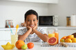 © Pixel-Shot - Little African-American boy with fresh juice and plate of different citruses sitting at table in kitchen