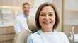 © liberty - Happy mature woman smiling in dental chair with dentist blurred in background