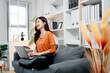 © Daenin - Young asian woman laughing and working remotely on laptop in a comfortable living room, enjoying her freelance lifestyle while achieving productivity and happiness at home