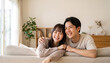 © Jesse_4160 - Happy young couple smiling and relaxing on a cozy sofa at home together, embracing warmth and love in a bright living room
