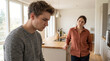 © ViskBx - Young man looking down with a sad expression while a woman stands in the background in a modern kitchen, representing relationship conflict