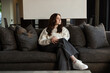 © Wavebreak Media - Female sitting on gray sofa in living room, wearing cream sweater and white sneakers