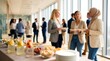 © CuteBee - Business professionals standing in office corridor during networking event having snacks and drinks with bright natural light through windows and blurred office background activity