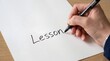 © Marina - A hand writes the word “Lesson” with a black pen on a white background. AI generated.