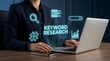 © Nogandranath - A professional business person working on a laptop computer with digital holographic icons representing search engine optimization and keyword research