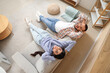 © Pixel-Shot - Young couple resting on grey sofa at home, top view