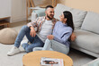 © Pixel-Shot - Young couple sitting near grey sofa at home