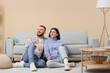 © Pixel-Shot - Young couple sitting near grey sofa at home