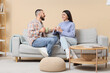 © Pixel-Shot - Young couple with cups of tea sitting on grey sofa at home