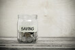 © mrzn - Glass jar labeled saving containing coins on a rustic wooden table surface with investment, financial