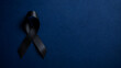 © Dzunstock - A black awareness ribbon on a dark blue background, symbolizing mourning, remembrance, or support for a cause.