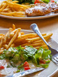 © CoreRock - Crisp french fry and fresh lettuce salad with creamy dressing and tomato pieces served with cutlery on wooden table, appetizing casual meal scene with golden fries and greens