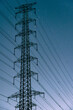 © GiangLe11 - Vertical close-up view of a majestic high voltage electrical transmission tower and diagonal power lines against a beautiful starry night sky with a deep blue gradient.