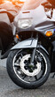 © HENADZY - Front view of parked sport motorcycle with grey and black body, showing wheel, brake disc, and suspension after rain, drops visible, sunlight reflection on upper part.