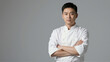 © Nikolay - Portrait of a professional Asian chef in a white uniform with a confident pose. Male cook standing against a grey background with ample copy space