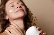 © SHOTPRIME STUDIO - A relaxed middle aged woman applies moisturizer on her face with eyes closed in a warmly lit room, highlighting natural beauty, selfcare, and authentic skin texture, calm confidence.