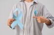 © Pixel-Shot - Young man with blue ribbons on light background, closeup. Prostate cancer awareness concept