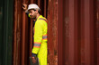 © KANGWANS - Logistics worker leaning against red cargo container at port shipping yard.  Freight Management, Port Operations, Thoughtful Supervision, Maritime Logistics