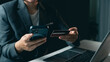 © PlengPleng - Business person using mobile phone and credit card for online payment or digital transaction in modern office workspace with laptop