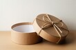 © miss irine - Round kraft paper box tied with jute twine sits open on a wooden table. Natural, eco friendly packaging for gifts or storage. Minimalist design, ready for content.
