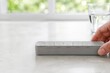 © Serjio - Mujer toca un objeto gris sobre una mesa con un vaso de agua al fondo