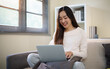 © matinee - Young Asian woman joining an online video call on a laptop while relaxing at home.