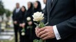 © Panpatsa - Adult in a suit holding a rose at an outdoor burial in a graveyard cemetery during a funeral service in grief.
